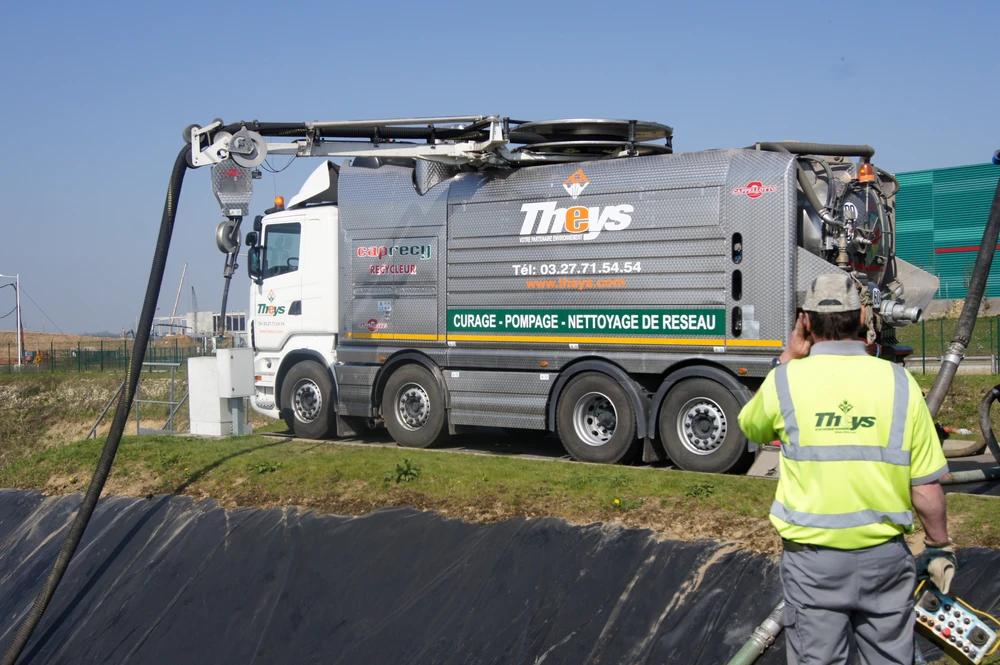 Camion hydrocureur Theys 8x4 sur chantier extérieur, opérateur en gilet haute visibilité supervisant l'opération