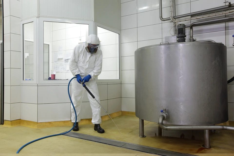 Technicien en combinaison de protection intégrale effectuant le nettoyage industriel d'un équipement de production dans une usine alimentaire