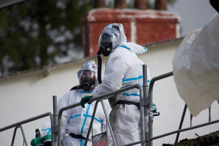 Scène extérieure urbaine avec deux techniciens en combinaisons de protection chimique blanches à bandes bleues, équipés de masques respiratoires complets noirs